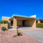 Front exterior of a classic 1970s burnt adobe townhome in Casa Real, Tucson, featuring a private carport and low-maintenance desert landscaping under a blue sky.
