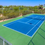 Blue tennis and pickleball court at Casa Real Townhomes in Tucson, Arizona, surrounded by green fencing and mature desert trees.