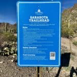 Blue Sarasota Trailhead sign at the entrance to Tucson Mountain Park, surrounded by saguaros and rugged Sonoran Desert hills in Tucson, Arizona.