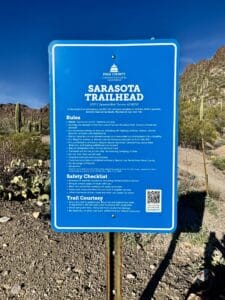 Blue Sarasota Trailhead sign at the entrance to Tucson Mountain Park, surrounded by saguaros and rugged Sonoran Desert hills in Tucson, Arizona.