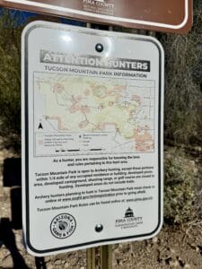 Hunting rules sign in Tucson Mountain Park showing archery hunting information and park regulations at a desert trail access point in Tucson, Arizona.